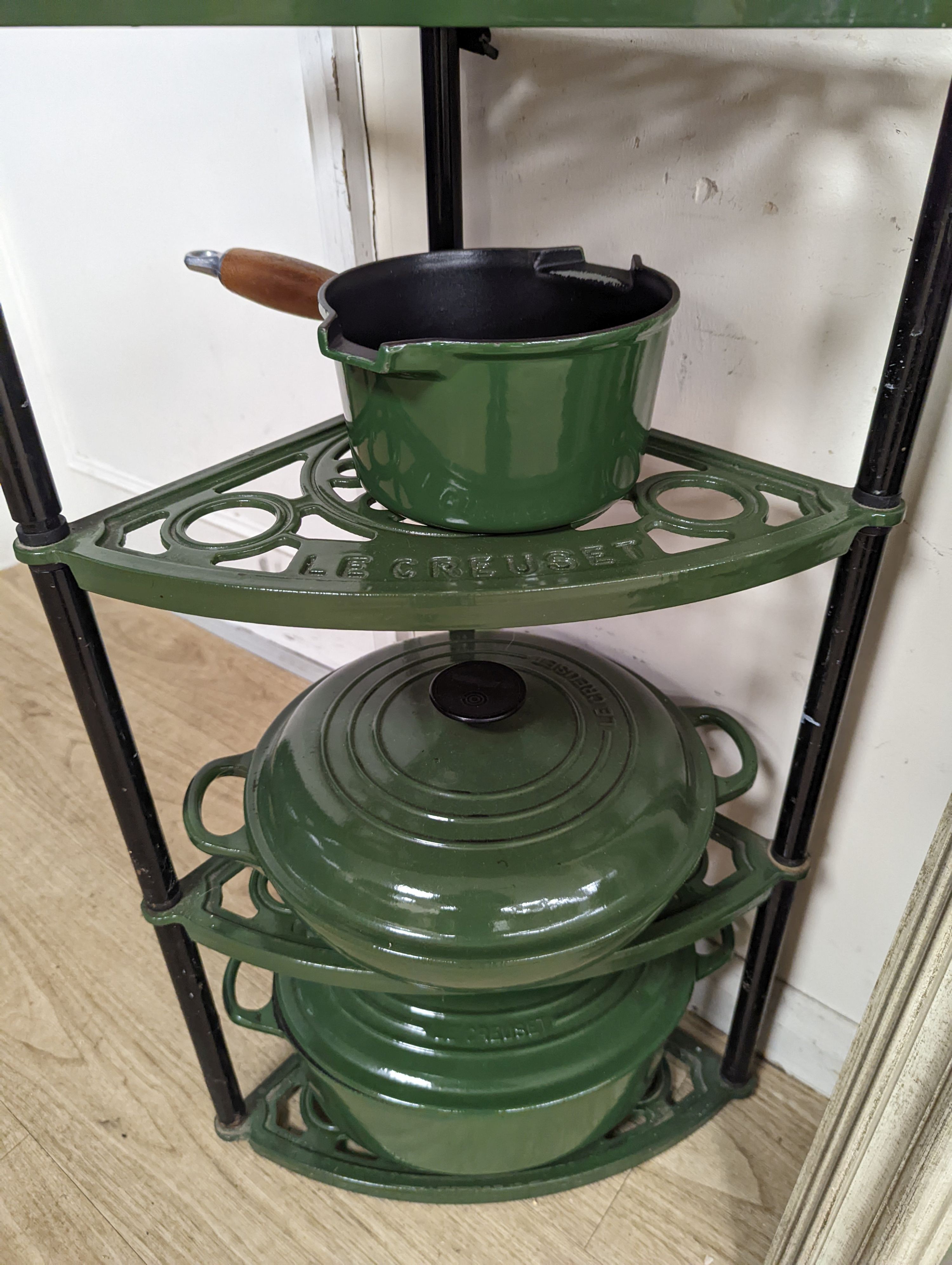 A green enamel Le Cruset pot stand, three pans and a bottle rack, stand 90 cms high.